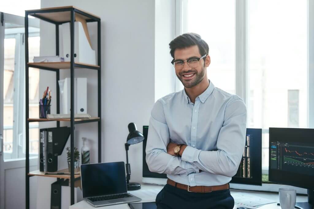 happy trader cheerful businessman in formal clothes and eyeglasses is keeping arms crossed smiling